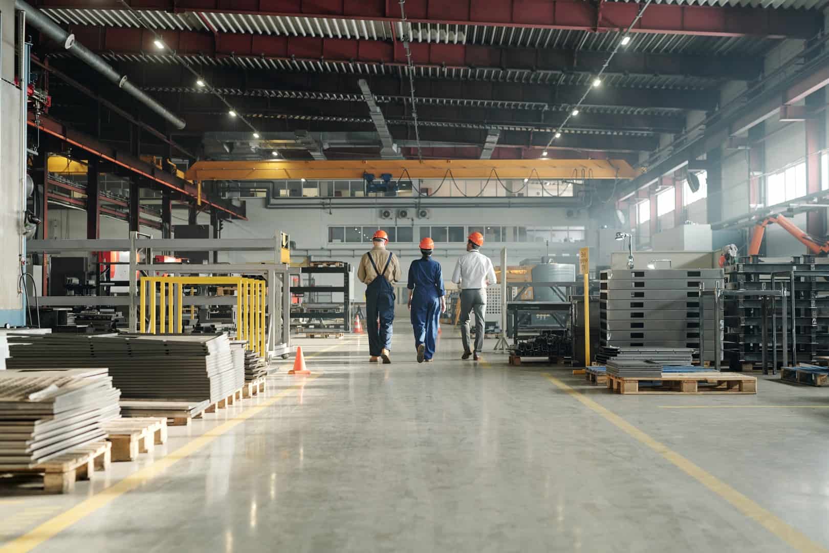 Rear view three technicians engineers industrial plant workwear leaving workshop end working day Large