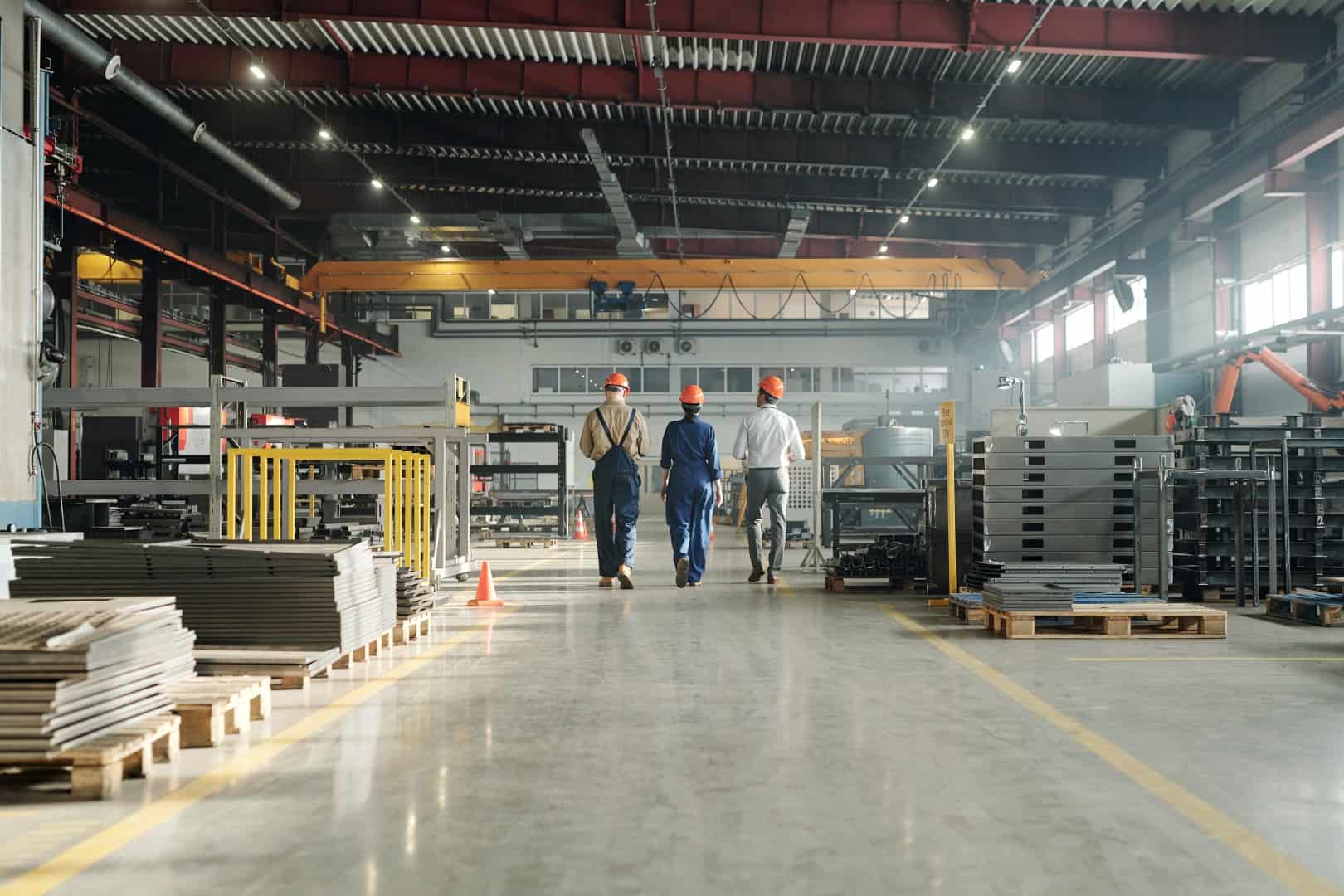 Rear View Of Three Engineers Leaving Workshop At The End Of Working Day